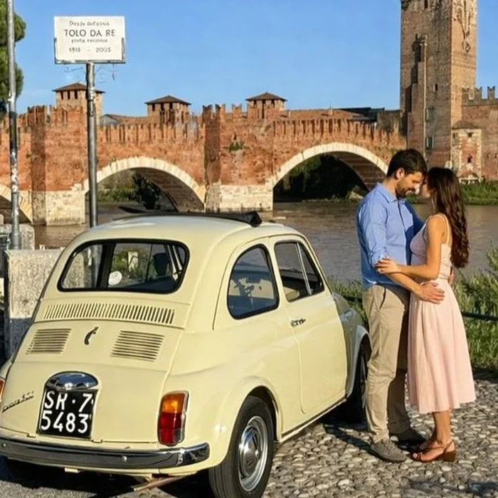 Una coppia si guarda accanto a una Fiat 500 crema, davanti al ponte di Castelvecchio a Verona, nella luce del tardo pomeriggio